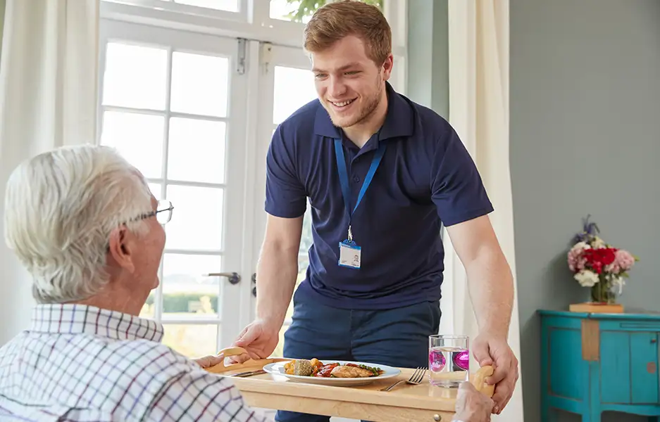 a young male carer serving an elderly man a meal